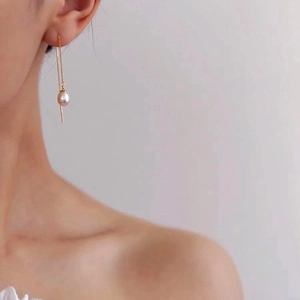 Close-up of long gold threader earrings with white teardrop freshwater pearls on model