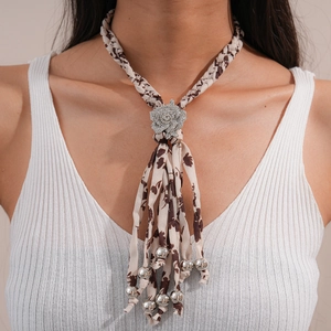 Gros plan d'un choker bohème en tissu avec boucle fleur en strass et pompons perlés