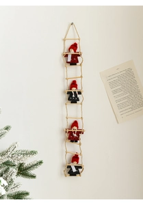 Detail of four felt Santa Claus figurines climbing a wooden ladder on a white wall