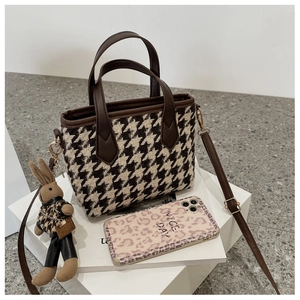 Détail du sac bandoulière pied-de-poule avec bordure en cuir brun et breloque lapin
