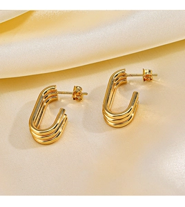 Macro shot of gold-plated triple-layer U-shaped earrings on elegant champagne silk fabric
