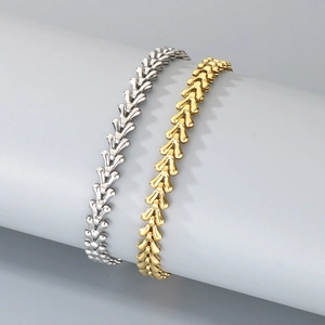 Detailed view of wheat chain bracelets in gold and silver finishes on a grey stand