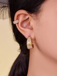 Macro view of gold flower earrings set and pavé zircon ear cuff worn by a model