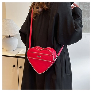 Detail of red heart-shaped crossbody bag with silver zippers shown on a model