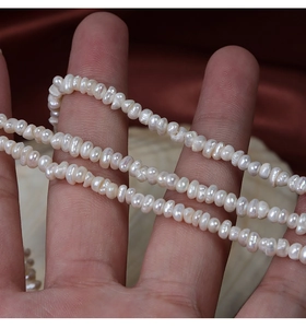 Vue macro de perles d'eau douce blanches irrégulières de 3-4mm sur les doigts pour la taille