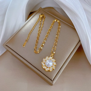 Dettaglio del ciondolo a fiore dorato con perla e zirconi su sfondo di seta elegante