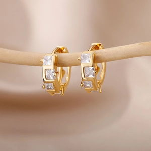 Detail of gold C-shaped hoop earrings with three square clear zircons on a branch