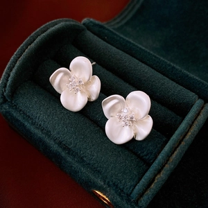 Detail of white matte flower earrings with zircon center in a dark green velvet jewelry box