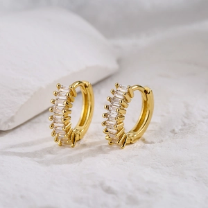 Gold-plated hoop earrings with baguette-cut zircon stones on a textured stone background