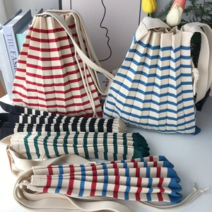 Detail showing various striped colors of knitted pleat bucket bags in a lifestyle setting