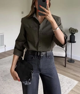 Detail view of a plaid long sleeve shirt paired with grey jeans and a leather bag