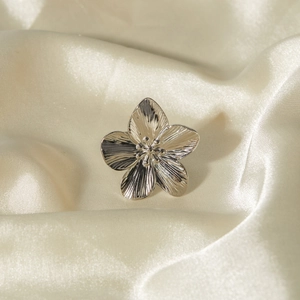 Détail d'une bague fleurie en acier argenté avec pétales texturés sur soie blanche