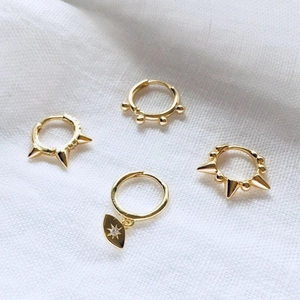 Detail of four gold hoop earrings with spikes and beads on white textured fabric
