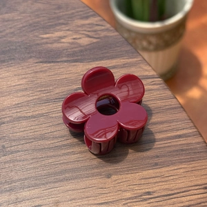 Gros plan sur une petite pince à cheveux fleur rouge foncé brillante sur surface en bois