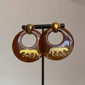 Détail de boucles d'oreilles créoles écaille avec motif panthère doré et clous en métal