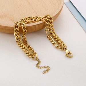 Double-layered gold chain bracelet with Figaro and Cuban links on a wooden tray