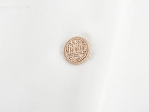 Macro shot of gold woven texture button on white fabric of elegant blazer