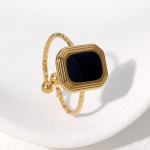 Textured gold square ring with black gemstone on a white ceramic plate