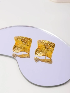 Macro shot of gold square hammered stud earrings with vintage wavy edges and reflections
