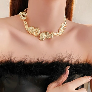 Close-up of chunky irregular lava-textured gold necklace on a black feathered outfit