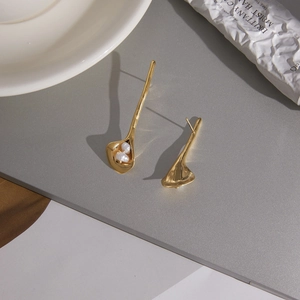 Detail of gold asymmetric calla lily earrings with freshwater pearls on a matte surface
