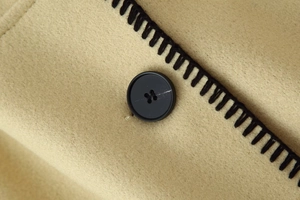 Close-up of beige wool coat featuring black contrast stitching and premium button detail