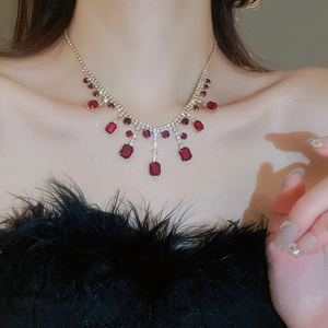 Detail of elegant gold necklace featuring a red square gemstone with fringe tassel pendant