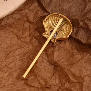 Detailed view of an 18K gold plated shell hairpin with a sparkling blue gemstone