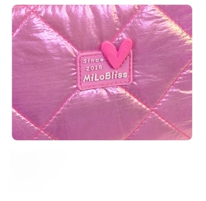 Macro shot of pink glossy quilted cosmetic bag featuring a heart rubber logo detail