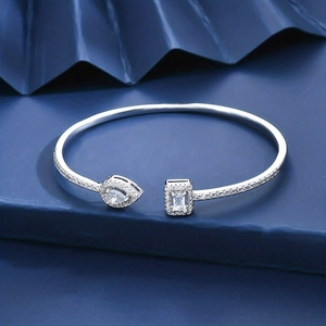 Macro shot of silver adjustable bangle with pear and rectangular stones on blue display
