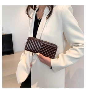 Gros plan du portefeuille en cuir verni marron avec matelassage en V tenu par un mannequin