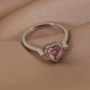 Detailed close-up of a silver ring with a pink heart-shaped gemstone on beige silk