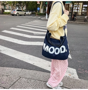 Outdoor street view of a navy blue denim crossbody bag with white MOOD lettering