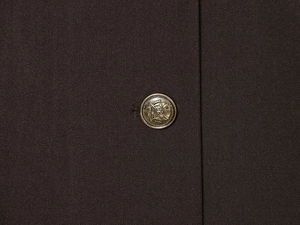 Dettaglio ravvicinato di tessuto twill marrone scuro con bottone in metallo dorato