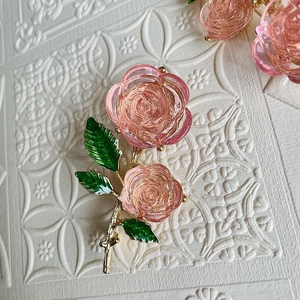 Vintage pink rose brooch with enamel green leaves and gold stem on white background