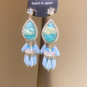 Macro detail of drop-shaped earrings with blue enamel, pearls and dangling bead tassels