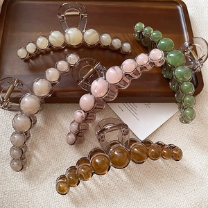 Elegant large resin hair claws in beige, pink, green, and amber colors on wood tray