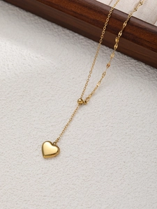 Dettaglio della collana con pendente a cuore dorato e catena sottile su fondo bianco