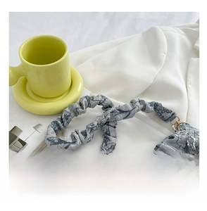 Detail of grey pleated shoulder bag with scrunchie strap and floral pendant charm
