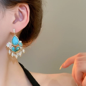 Detailed close-up of luxurious turquoise and pearl tassel earrings on a model's ear