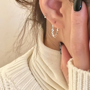 Close-up of geometric faceted silver hoop earrings worn with white knit sweater