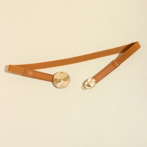 Detail of camel elastic belt with a golden circular embossed metal buckle on white leather
