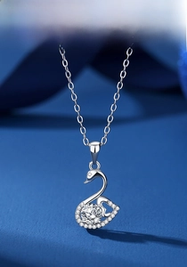 Macro shot of silver swan pendant with sparkling zircon wings on textured blue background