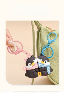 Detail showing two cute penguin keychains in pink and blue on a textured green bag