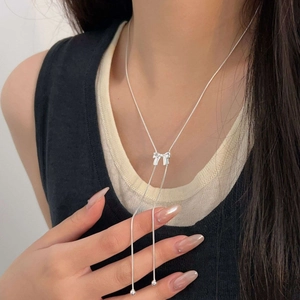 Close-up of a silver bow pendant necklace with bead accents on a model's neckline