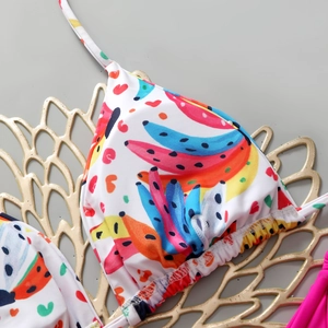 Detail view of white bikini top with colorful abstract banana print on elegant gold tray