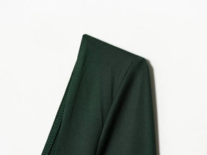 Detail view of dark green knit fabric texture and double-stitch seam of the bodysuit