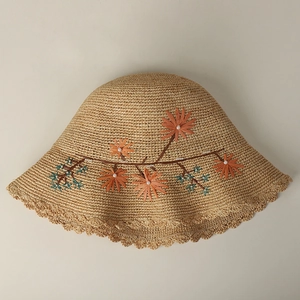 Detailed embroidery of orange raffia flowers and white faux pearls on woven straw hat