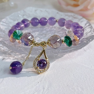 Macro shot of natural amethyst bracelet with zircon flower and gold pendant in glass dish