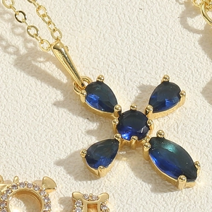 Macro view of gold plated cross necklace featuring a deep blue zircon gemstone inlay